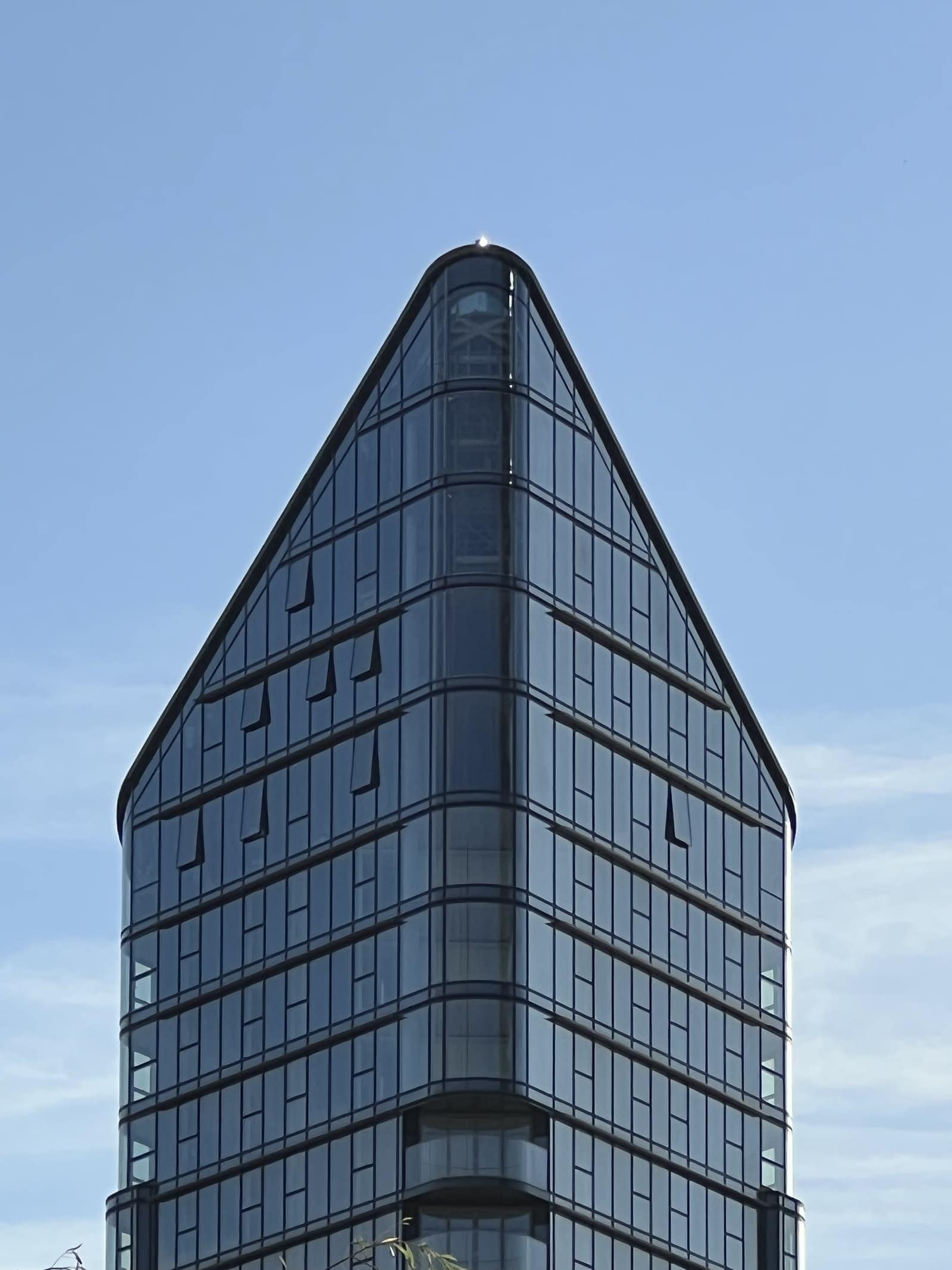 A tall angular glazed tower photographed from street level against a clear sky